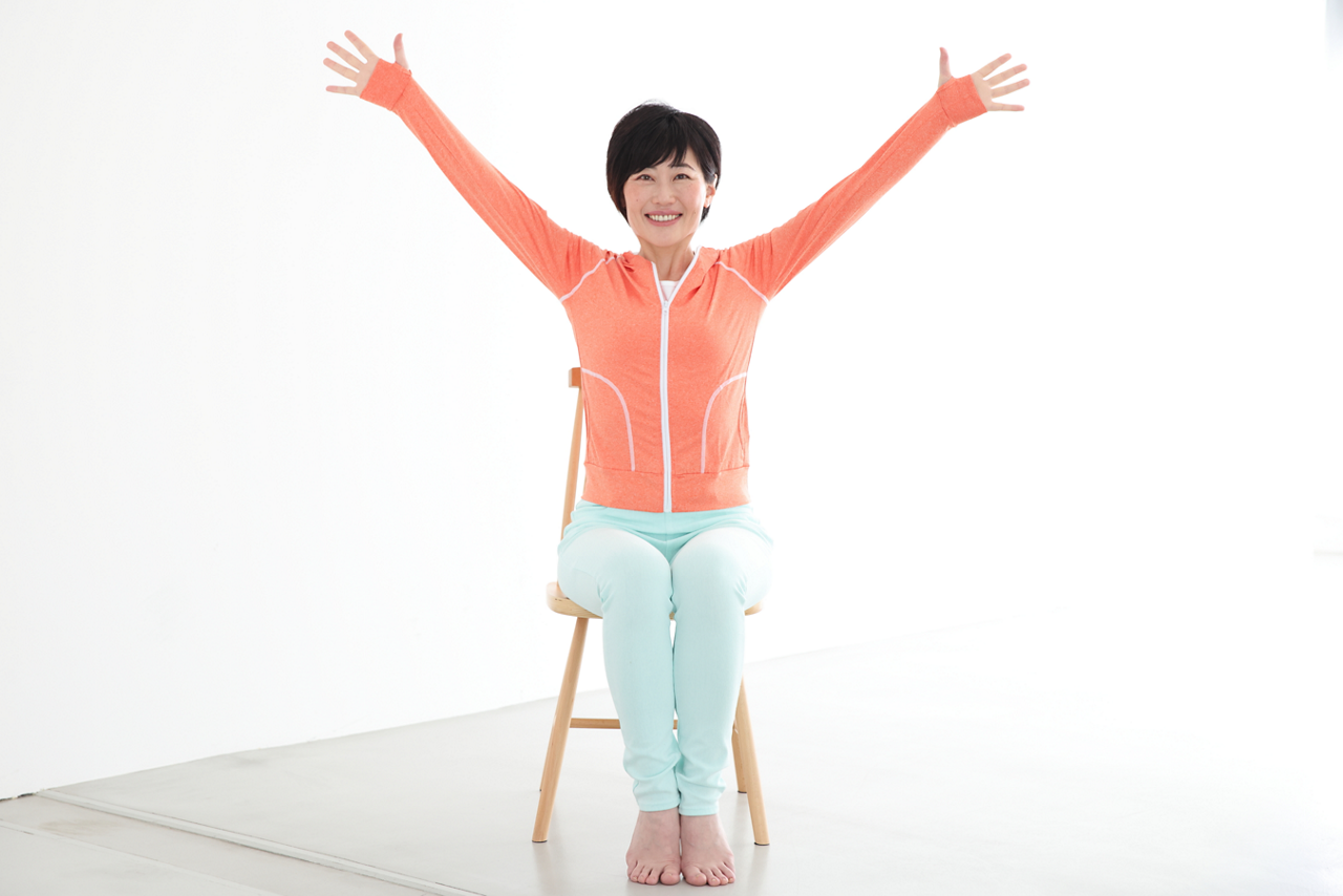 やる気アップ対策＜その2＞やる気も代謝もアップする体操。①膝をそろえていすに座り、顔を正面に向け、笑顔で両手を斜め上に上げる。