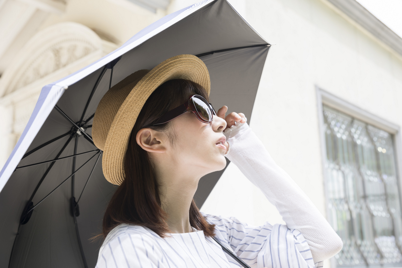 炎天下で活動する場合に気をつけること。UVカット機能のある衣類や帽子、サングラス、日傘、化粧品などを活用し、強い紫外線を避ける人物のイメージ画像